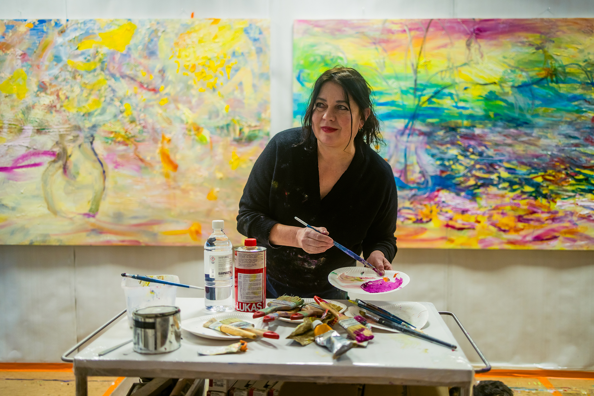 Nanna Susi studiossaan paletin ja maalausten ääressä